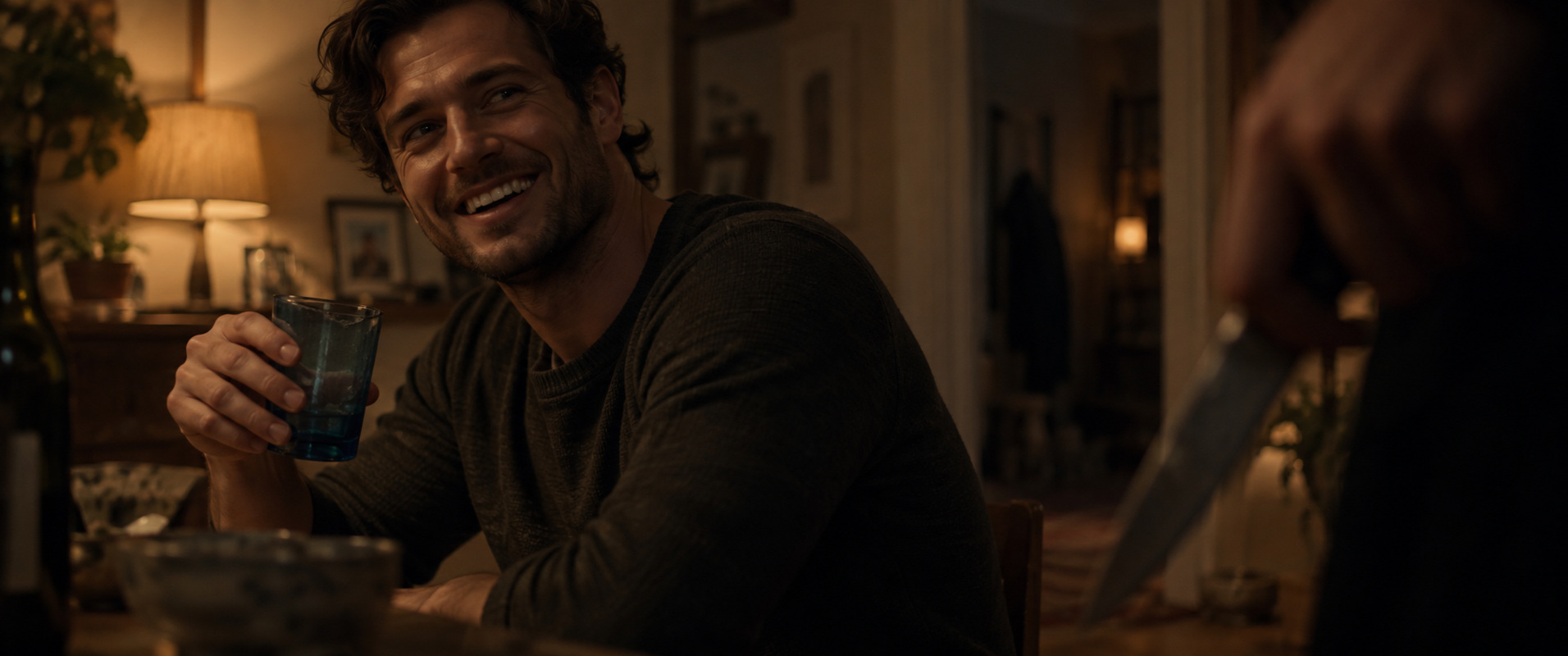 Kaden laughing in a warm kitchen, holding his chipped blue drinking glass.