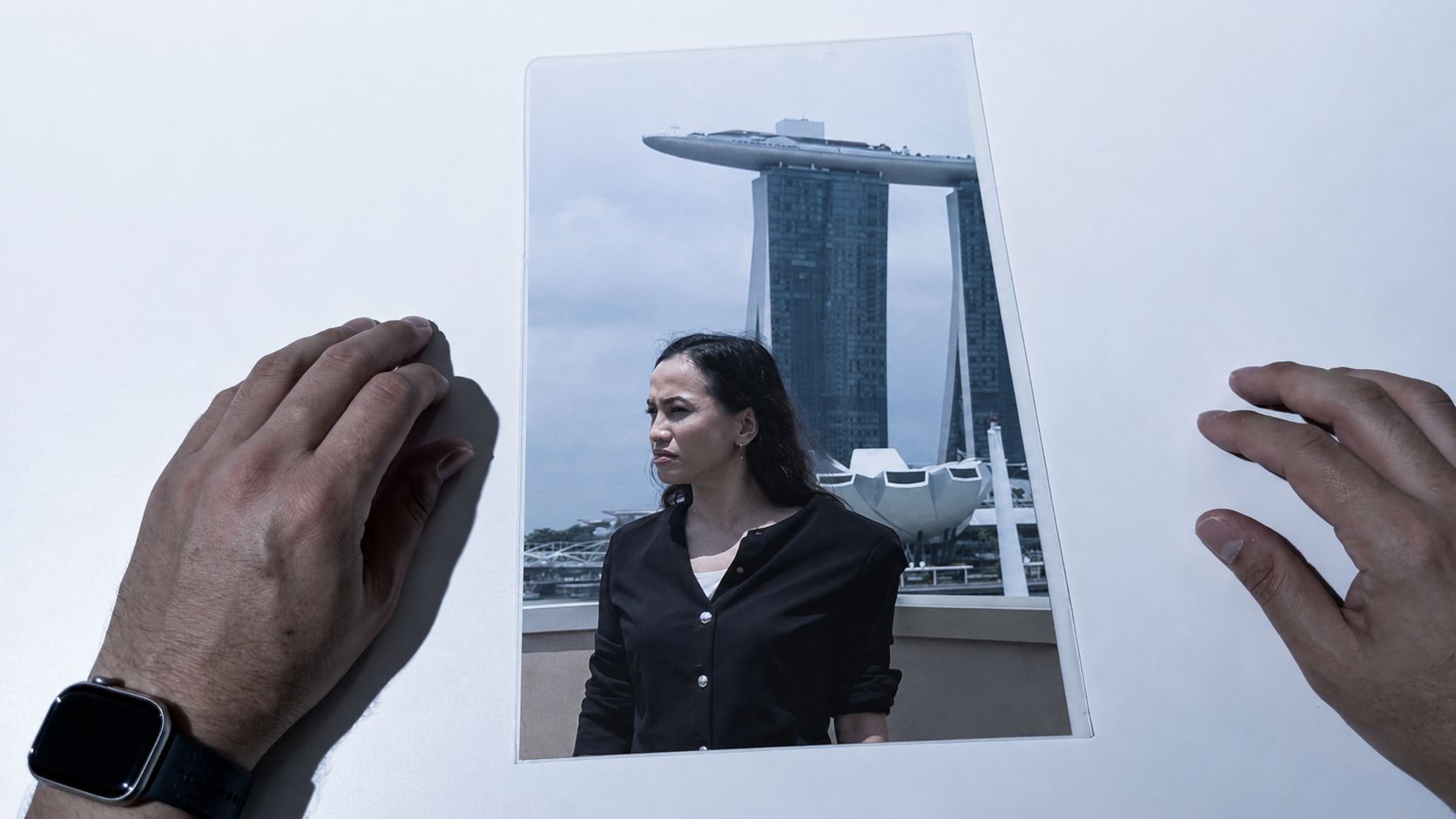 The same hands holding the card, which now shows a photograph of a woman on a city rooftop.